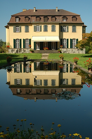 Im historischen Wasserbecken spiegelt sich das Schloss im Queen-Auguste-Victoria-Park
